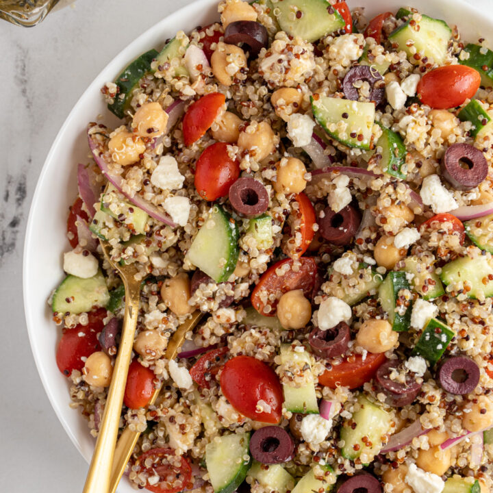A white bowl with greek quinoa chickpea salad with serving spoons.