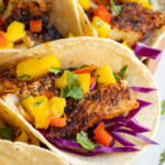 Pinterest pin with text over lay "Blackened Fish Tacos with Mango Salsa", image of blackened fish tacos with mango salsa on a tray.