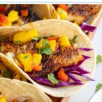 Pinterest pin with text over lay "Blackened Fish Tacos with Mango Salsa", image of blackened fish tacos with mango salsa on a tray.