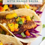 Pinterest pin with text over lay "Blackened Fish Tacos with Mango Salsa", image of blackened fish tacos with mango salsa on a tray.