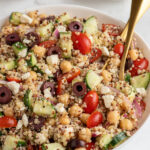 Pinterest pin with text overlay "Greek Quinoa Chickpea Salad", image of a white bowl filled with greek quinoa salad with chickpeas.