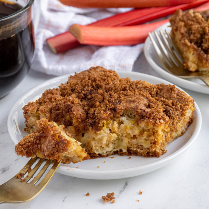 A plate with a slice of rhubarb coffee cake with a fork with a bite on it ready to be eaten.