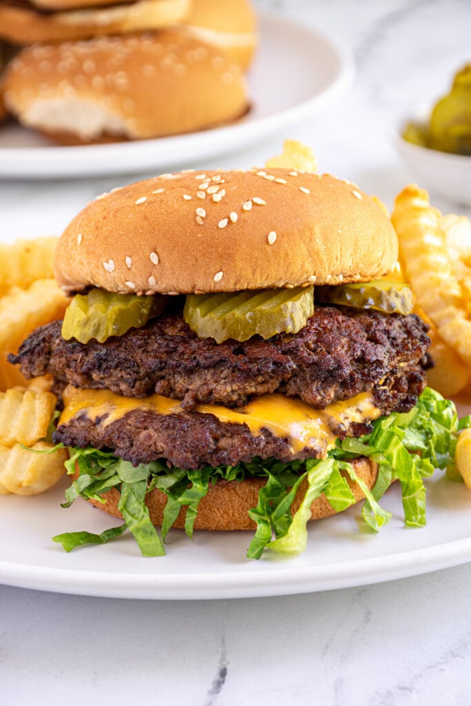 Close up of a smash burger made on the blackstone in a bun with lettuce and pickles on a plate.