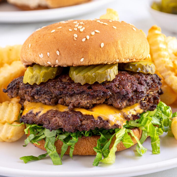 Close up of a smash burger made on the blackstone in a bun with lettuce and pickles on a plate.