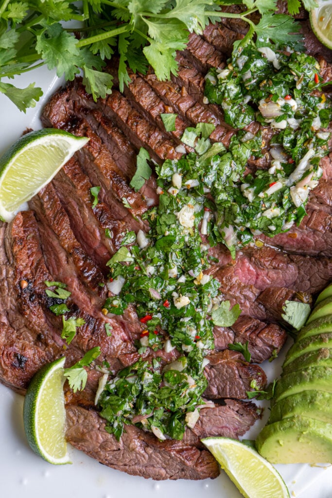 Chimichurri sauce overtop grilled meat showing off the bright green herbs and spices in olives oil.