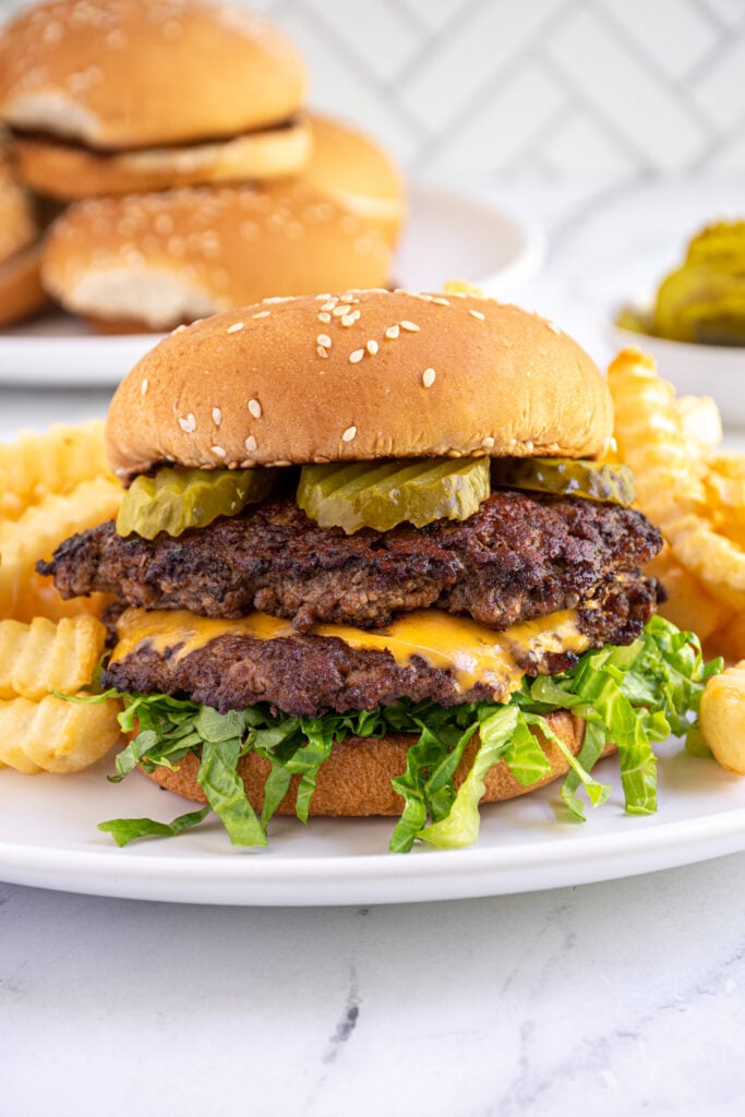 A smash burger made on a blackstone grill in a bun with lettuce and pickles.