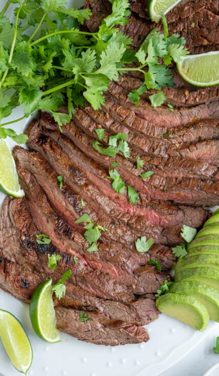 Carne asada steak sliced up to reveal the tender juicy insides garnished with cilantro and limes.