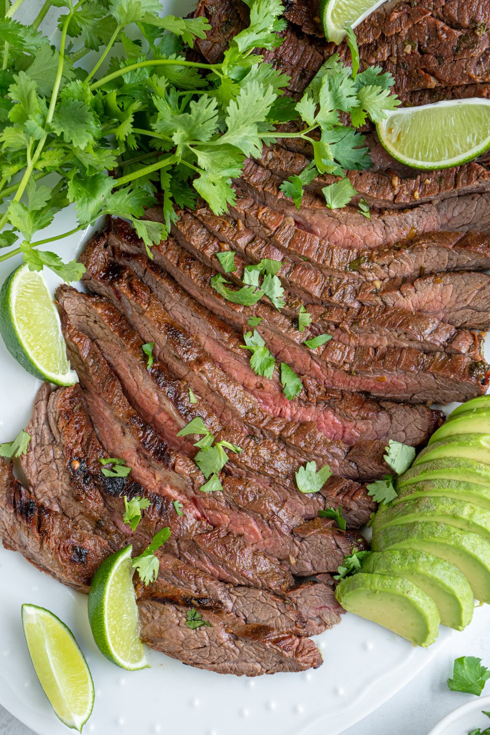 Carne asada steak sliced up to reveal the tender juicy insides garnished with cilantro and limes.