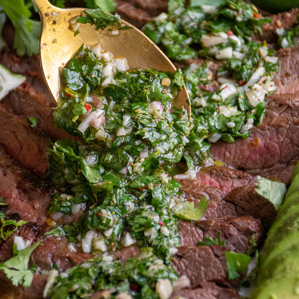 Bright green Chimichurri sauce being spooned onto grilled meat.