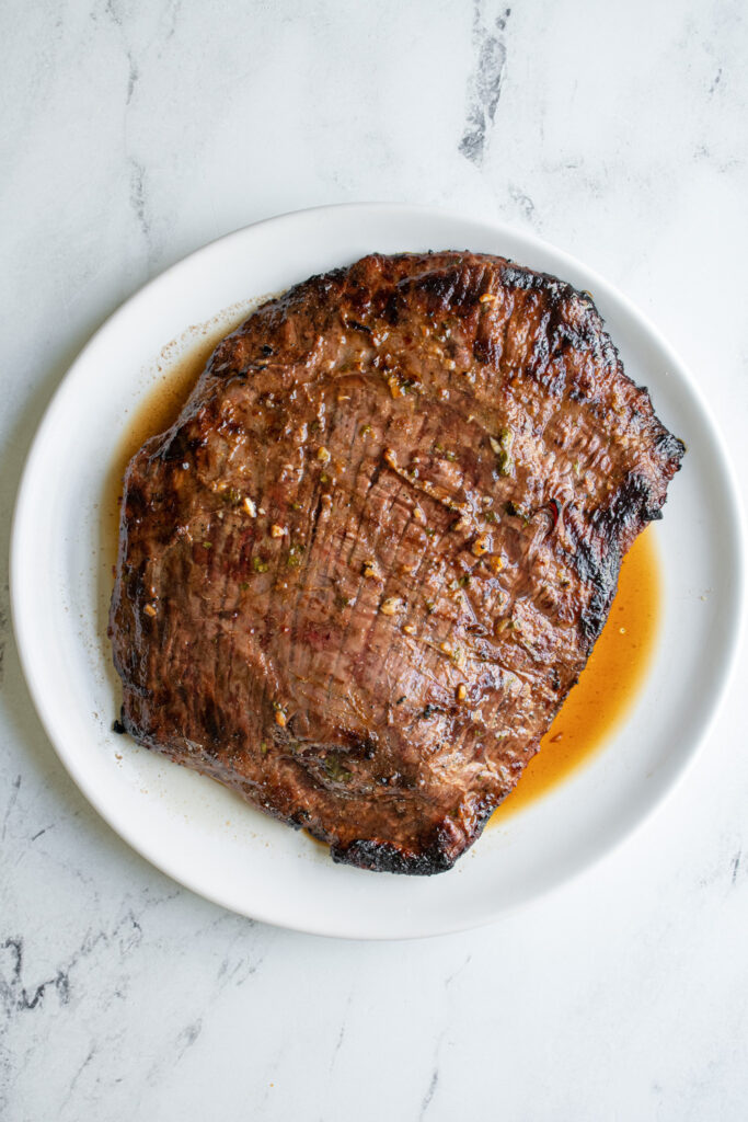 Carne asada fresh off the grill on a white plate after resting.
