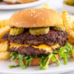 Pinterest pin with logo overlay "The Schmidty Wife" with the image of a double smash burger in a bun with lettuce and pickles.