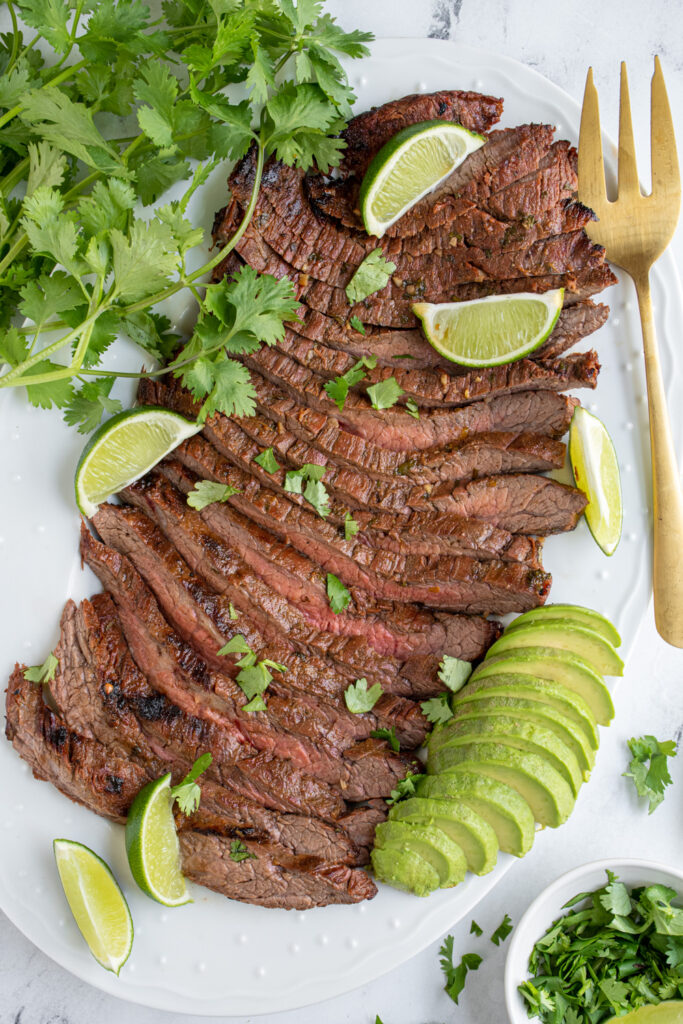 A white platter full of sliced carne asada steak.