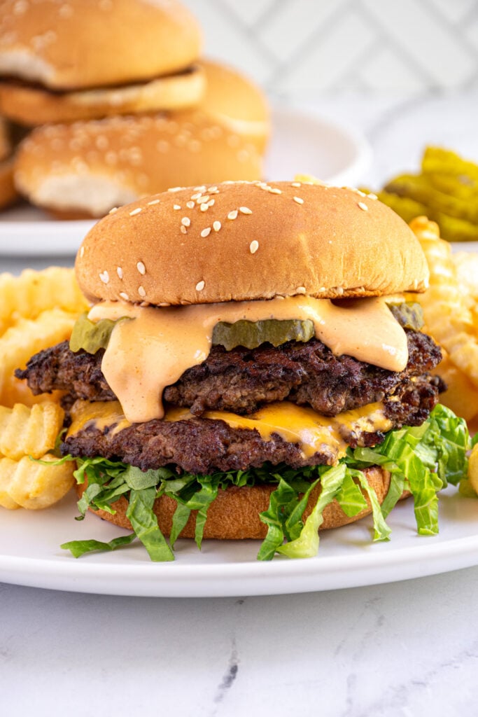 A double smash burger made on the blackstone in a bun with lettuce, pickles, and bug Mac sauce dripping down.