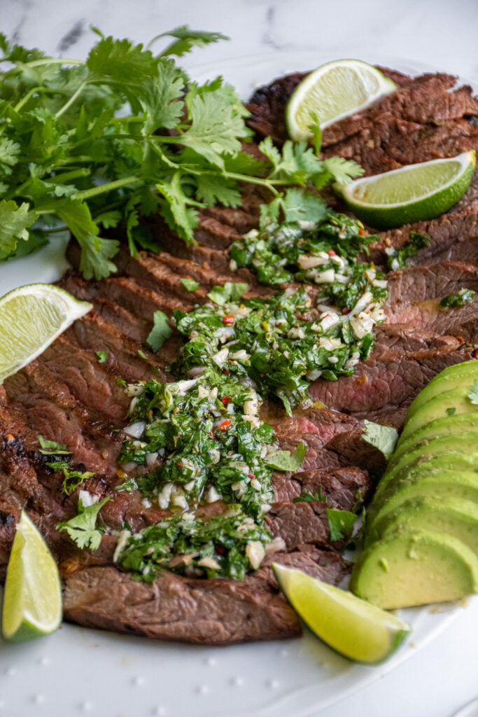 Green chimichurri recipe overtop grilled steak on a platter.