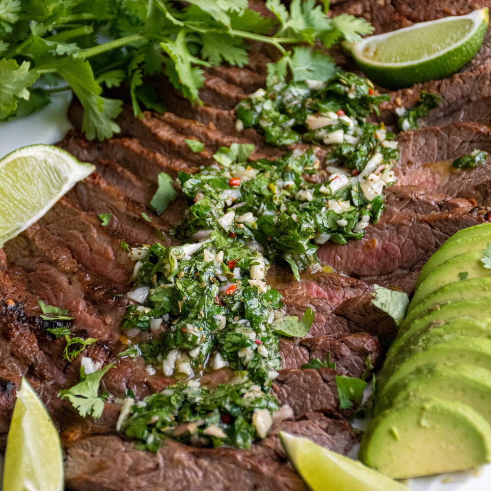 Green chimichurri recipe overtop grilled steak on a platter.