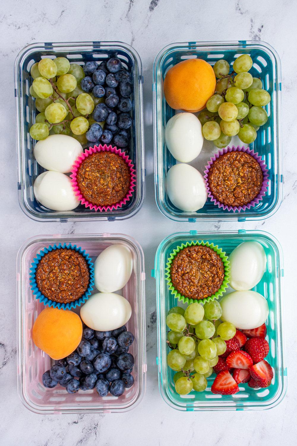 Four breakfast boxes on a tabletop each with hard boiled eggs, muffin, and fruit.
