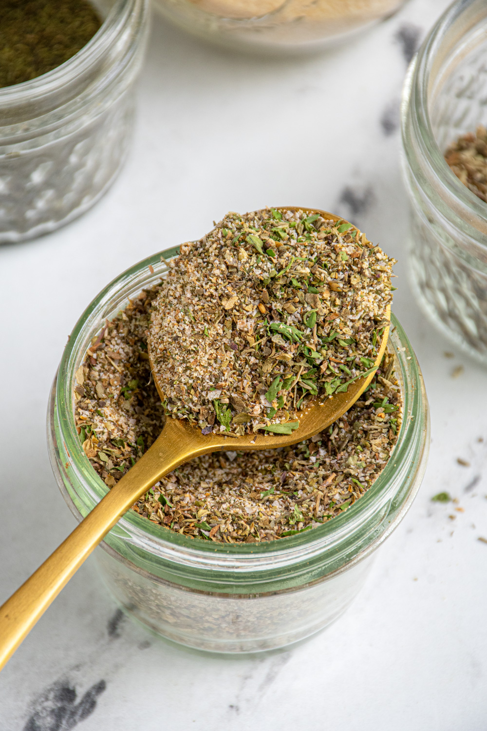 A jar with a spoon resting on top filled with homemade greek seasoning recipe.