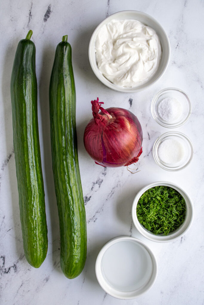 Ingredients to make creamy cucumber salad laid out on a table top.