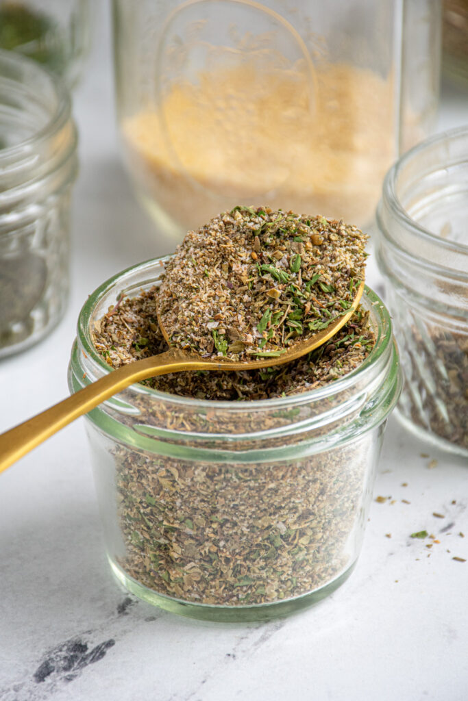 A jar with a spoonful of greek seasoning.