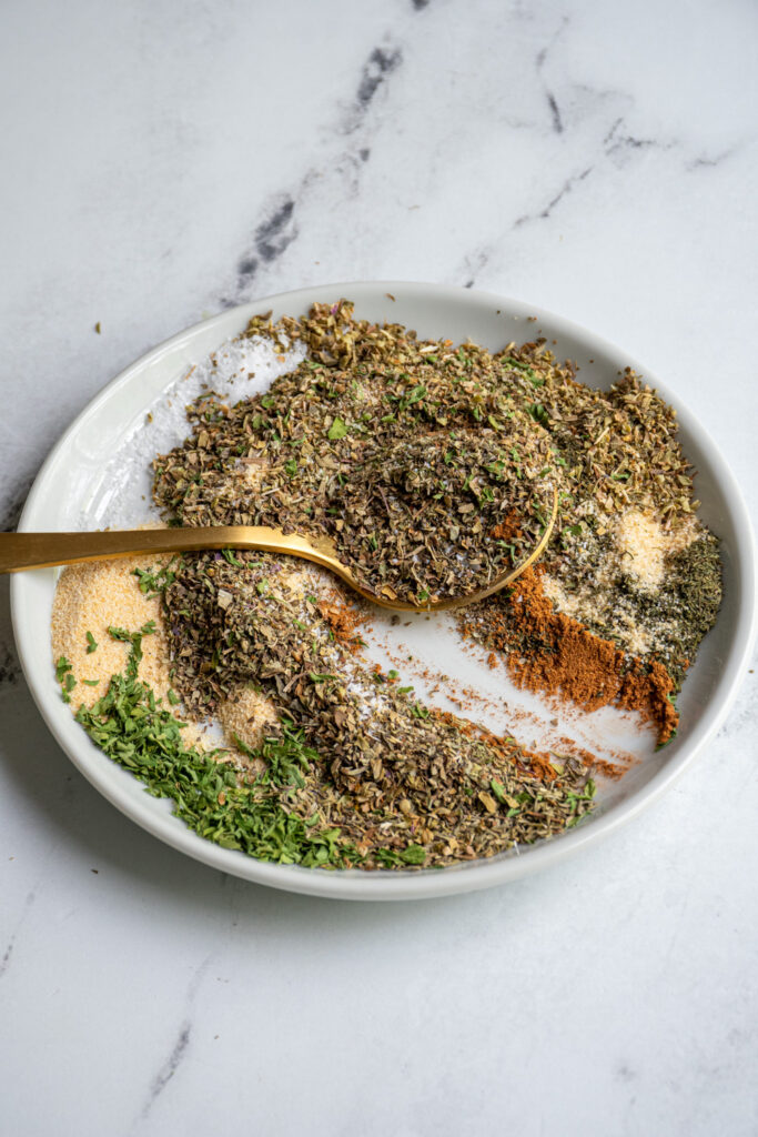 Mixing together the spices that make up greek seasoning on a plate.