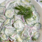 Pinterest Pin with text overlay "Creamy Cucumber Salad" image of a white bowl filled with creamy cucumber salad with dill.