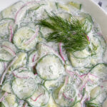 Pinterest Pin with text overlay "Creamy Cucumber Salad" image of a white bowl filled with creamy cucumber salad with dill.
