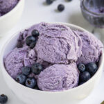 Pinterest pin with text overlay "Homemade Blueberry Ice Cream", image of a bowl with scoops of blueberry ice cream and fresh blueberries.