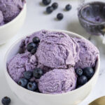 Pinterest pin with text overlay "Homemade Blueberry Ice Cream", image of a bowl with scoops of blueberry ice cream and fresh blueberries.