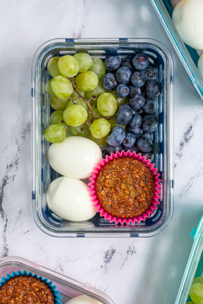 An overhead view of a breakfast bistro box with hard boiled eggs, a muffin, and fruit.