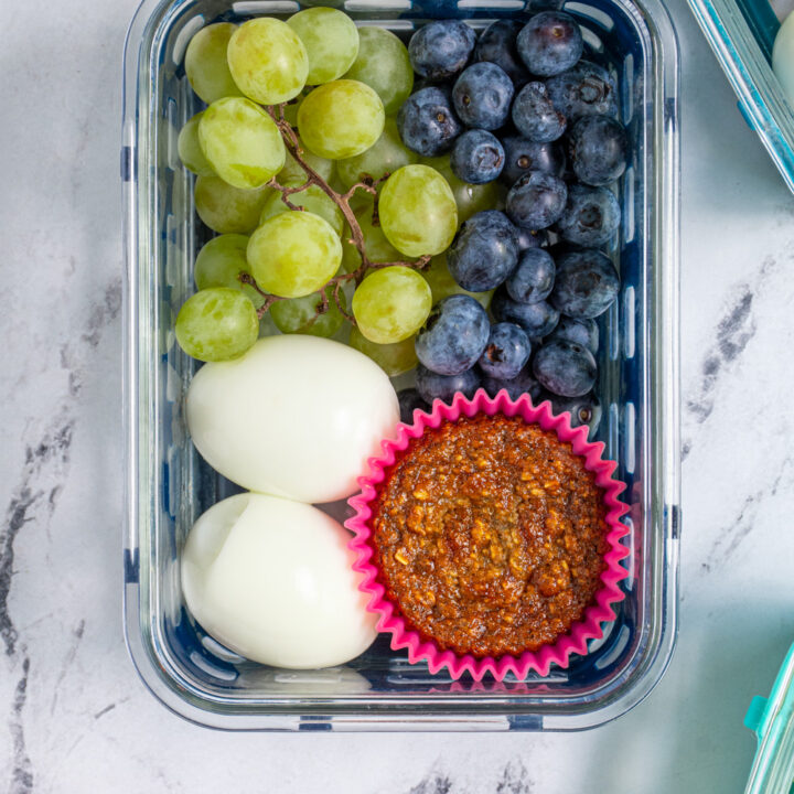 An overhead view of a breakfast bistro box with hard boiled eggs, a muffin, and fruit.