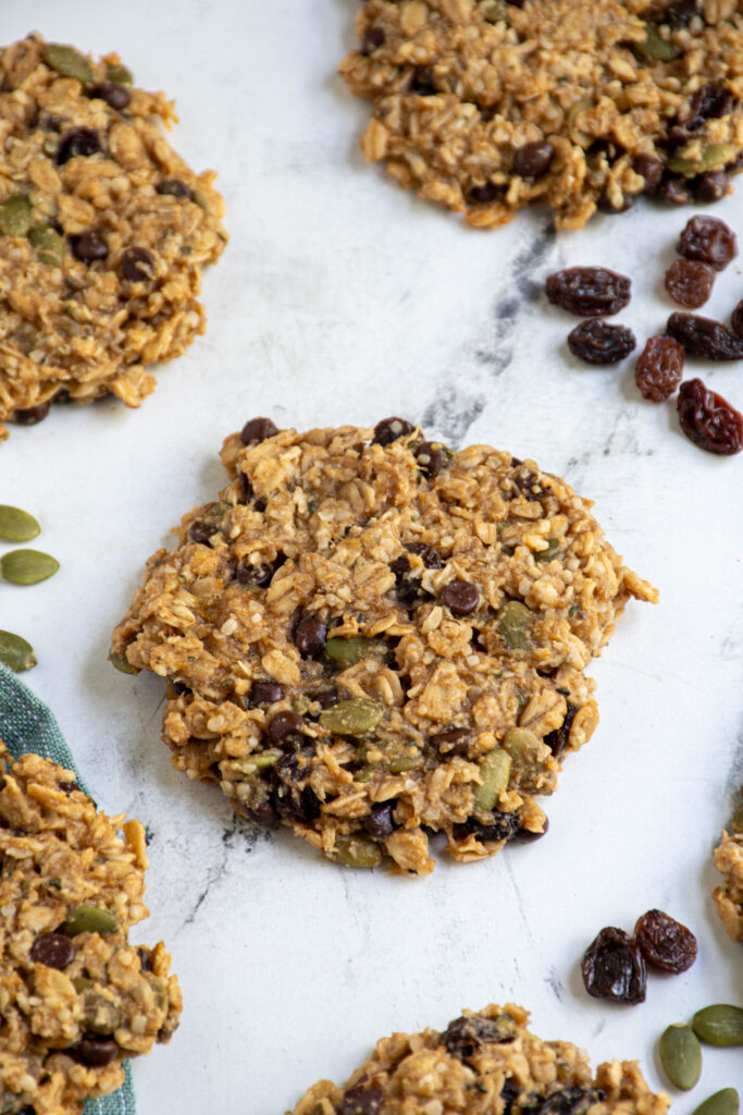 Breakfast cookies on a tabletop with one in the center showing off fillings like raisins, pumpkin seeds, and mini chocolate chips.