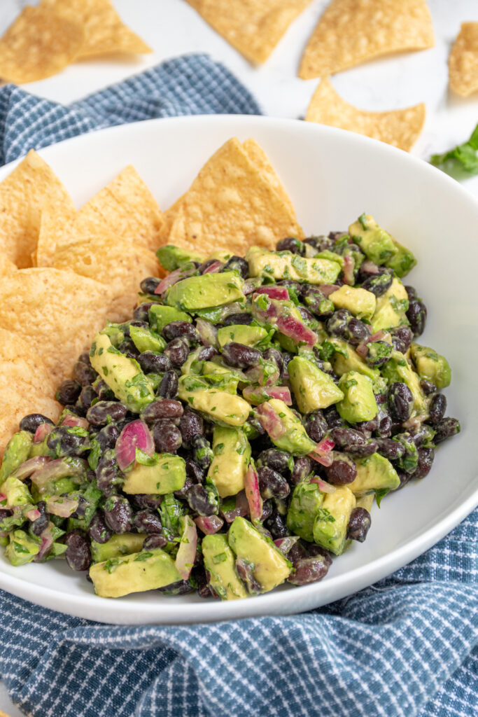 A white bowl with tortilla chips and avocado black bean salsa with pickled red onions.