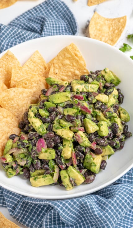 A white bowl with tortilla chips and avocado black bean salsa with pickled red onions and cilantro.