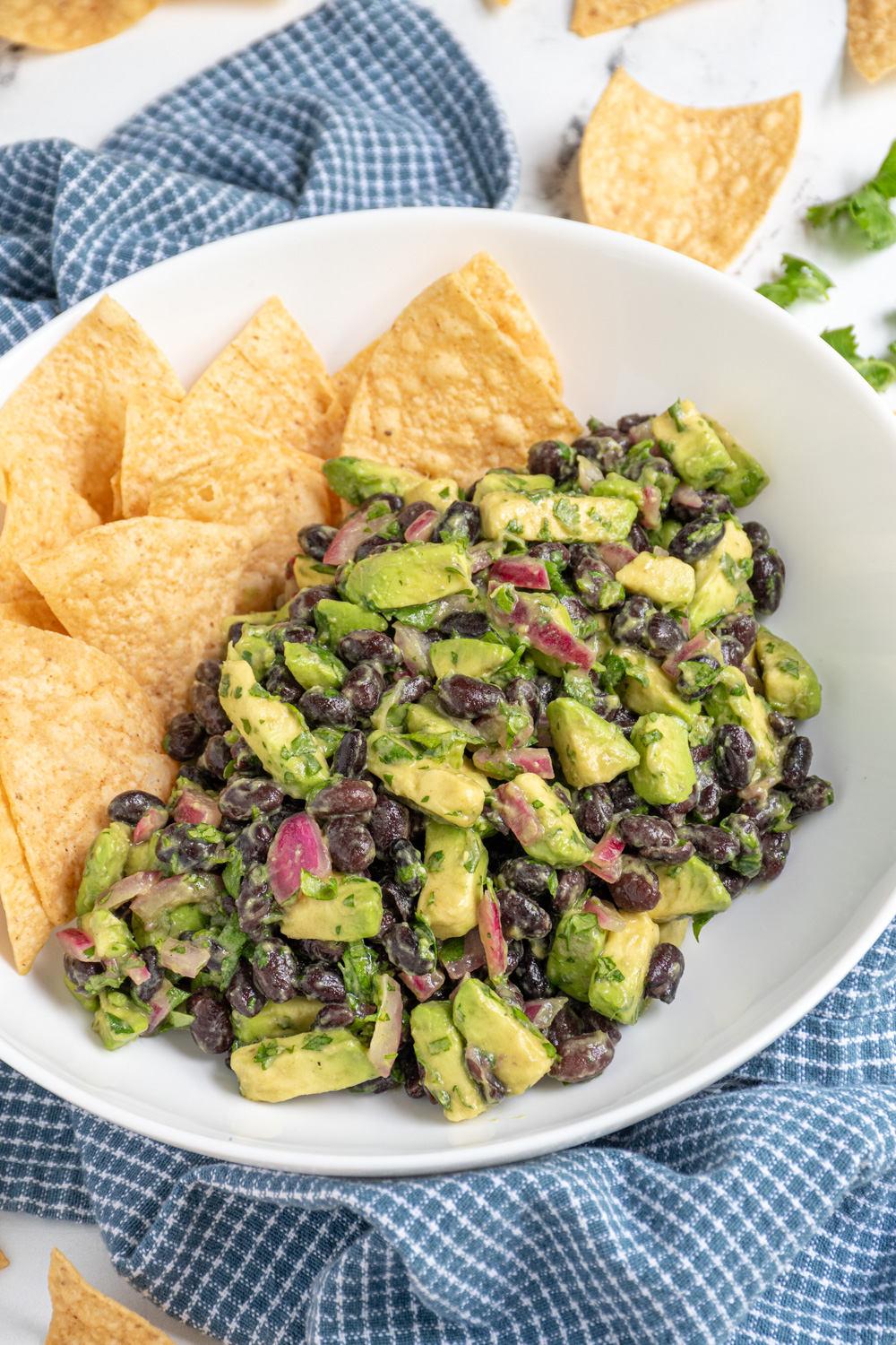 A white bowl with tortilla chips and avocado black bean salsa with pickled red onions and cilantro.