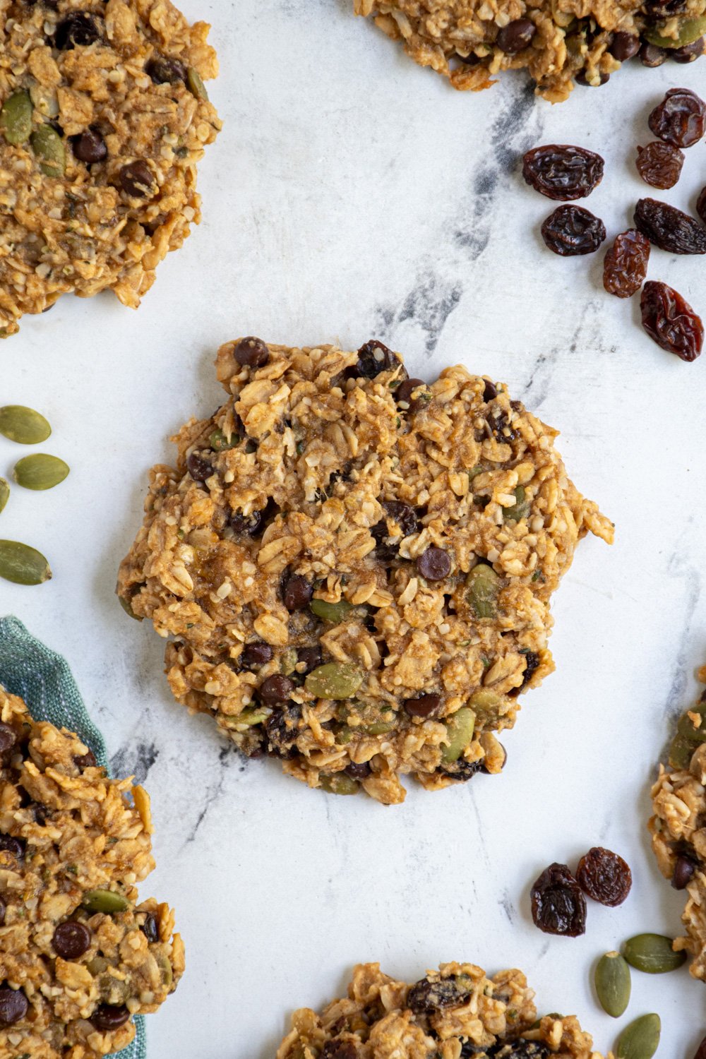 A breakfast cookie laying on a tabletop made up of oats, seeds, and raisins.