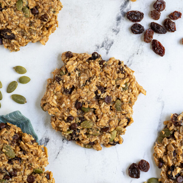 Breakfast cookies laid out on the table with one in the center filled with add-ins like seeds and raisins.