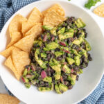 Pinterest Pin with image of a white bowl with black bean avocado salsa and tortilla chips.
