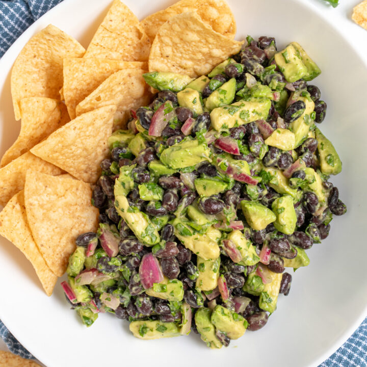 White bowl with avocado black bean salsa and tortilla chips.