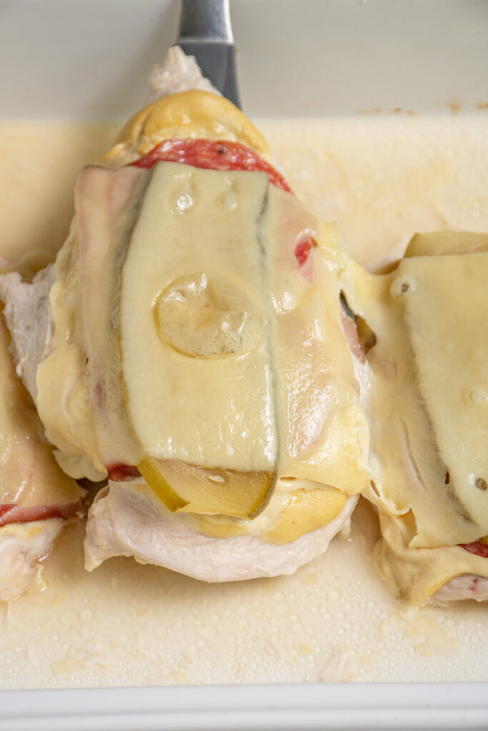 A spatula serving cubano chicken from a serving dish pulling up melty swiss cheese.