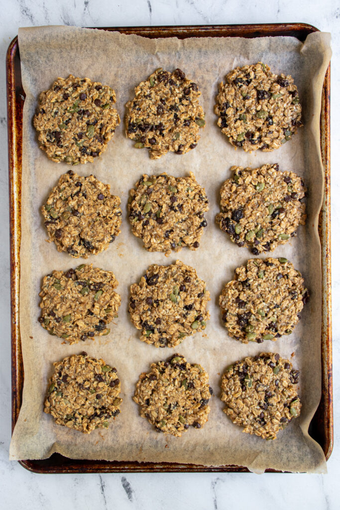 A sheet pan with apartment paper with 12 freshly baked banana oat breakfast cookies.