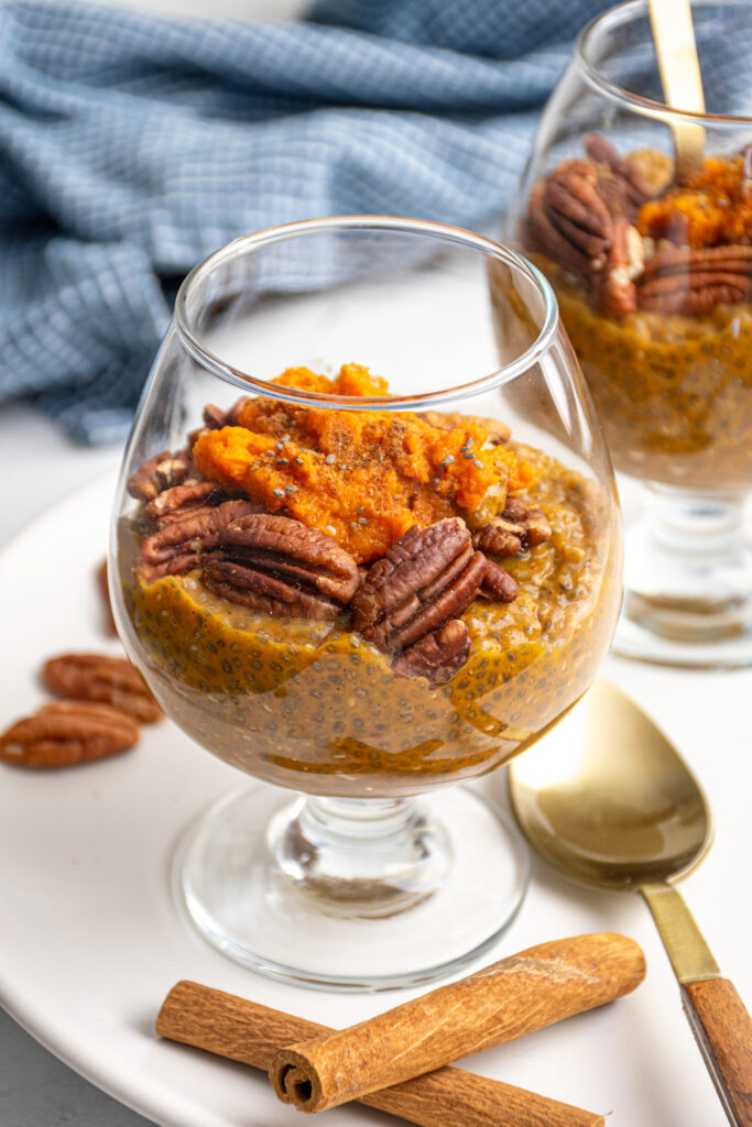 A glass with orange colored pumpkin chia seed pudding topped with pecans and pumpkin puree.
