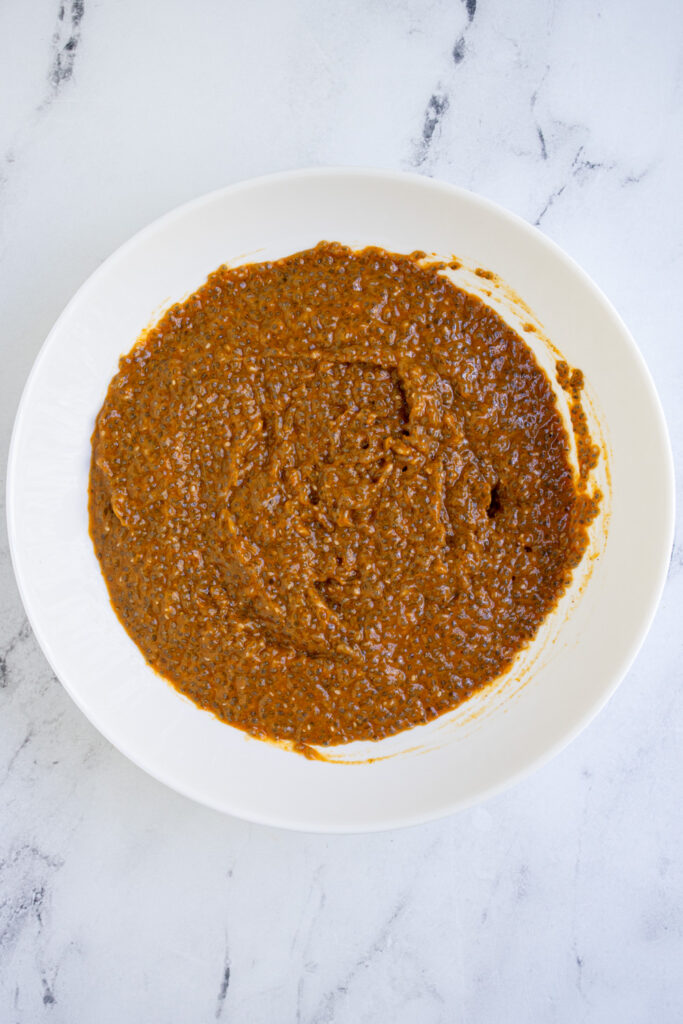 A white bowl with orange colored freshly made pumpkin chia seed pudding.