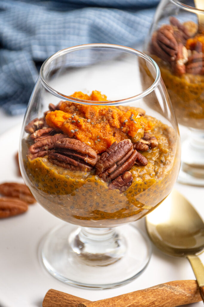 Close up of pumpkin chia seed pudding in a clear glass topped with pecans and pumpkin puree.