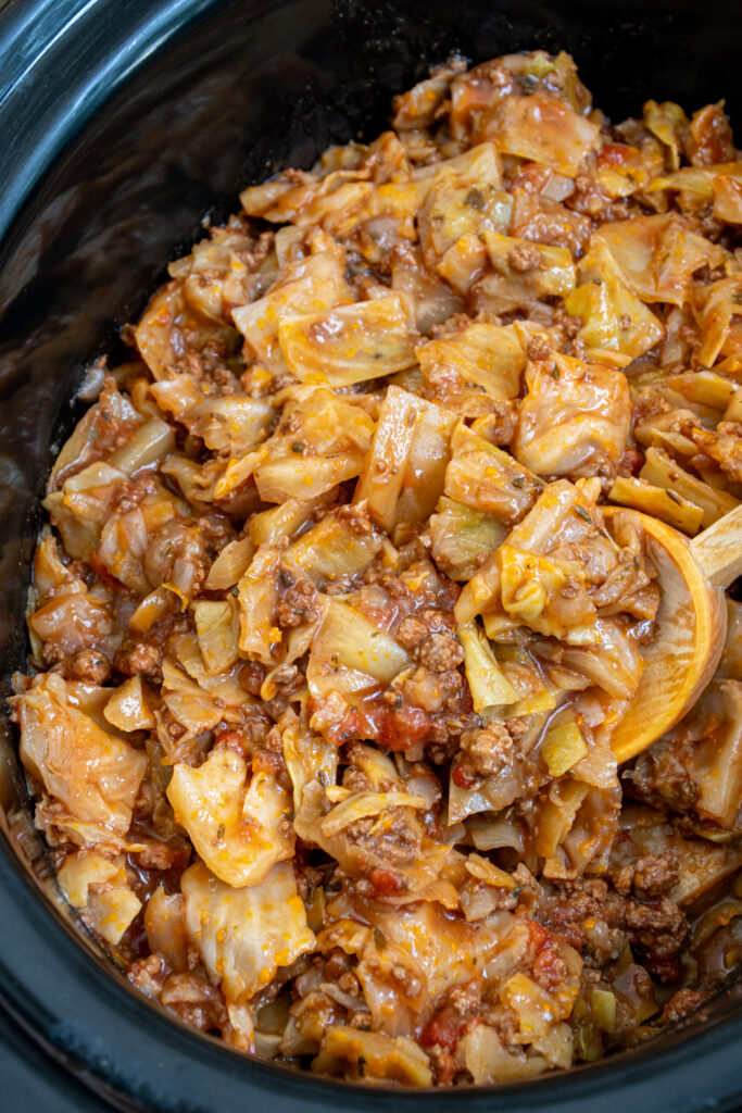 Close up of a crockpot with unstuffed cabbage rolls and a wooden spoon.