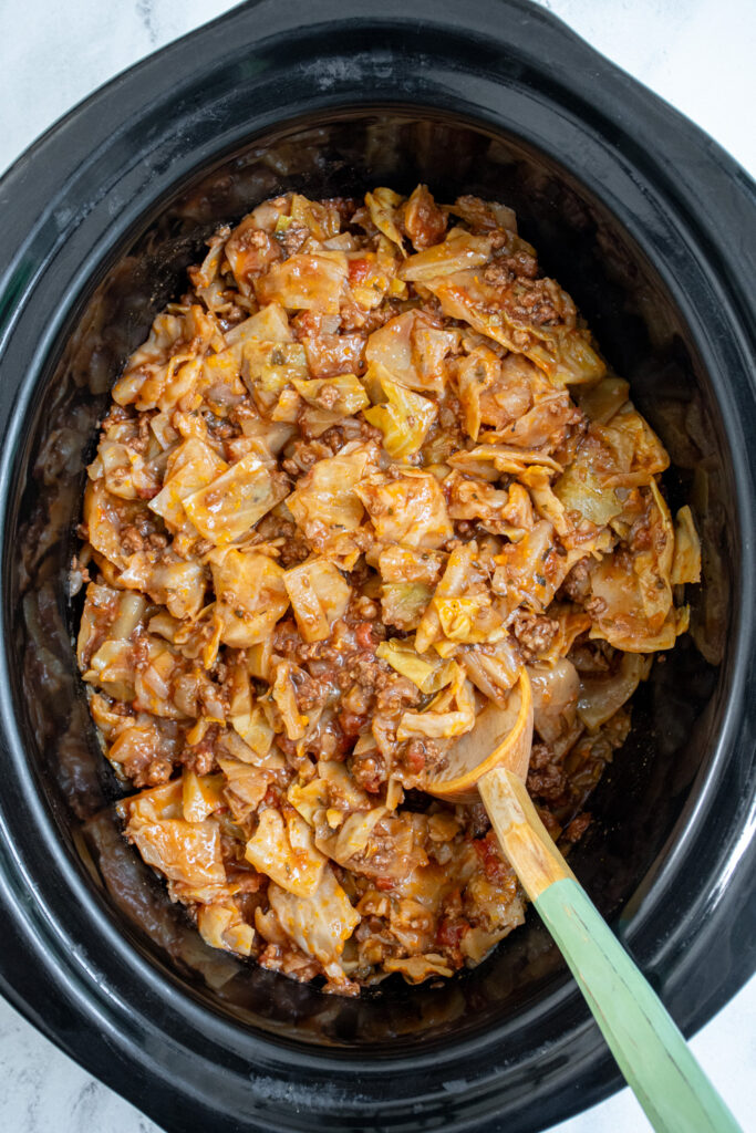 Crockpot with a wooden spoon in unstuffed cabbage rolls.