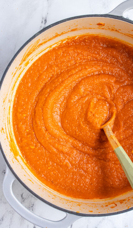 A large gray pot filled with butternut pasta sauce with a large wooden spoon for serving.