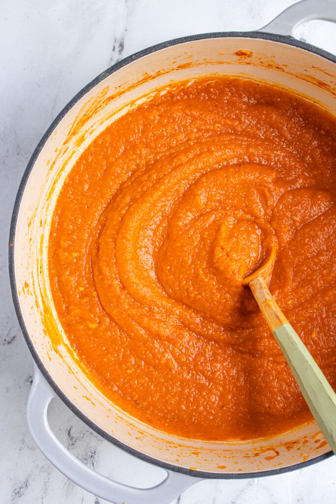 A large gray pot filled with butternut pasta sauce with a large wooden spoon for serving. 