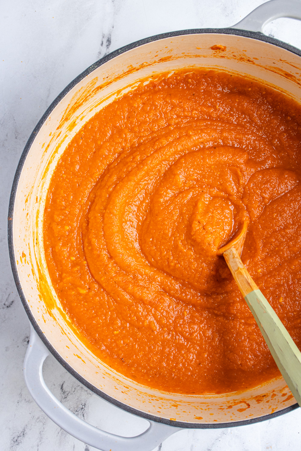 A large gray pot filled with butternut pasta sauce with a large wooden spoon for serving.