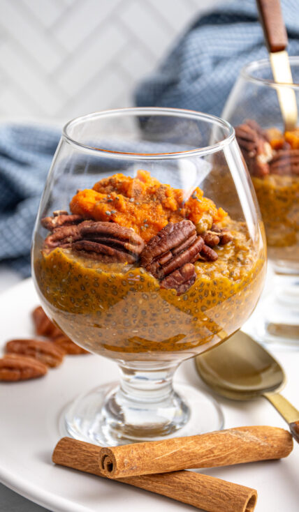 A glass with orange colored pumpkin chia seed pudding topped with pecans and pumpkin puree.