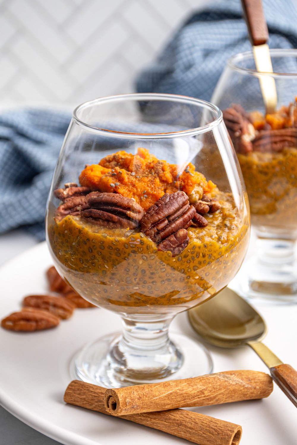 A glass with orange colored pumpkin chia seed pudding topped with pecans and pumpkin puree.
